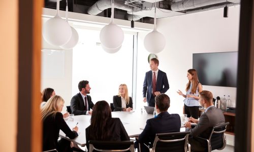 Group Of Young Businessmen And Businesswomen Meeting Around Table At Graduate Recruitment Assessment Day